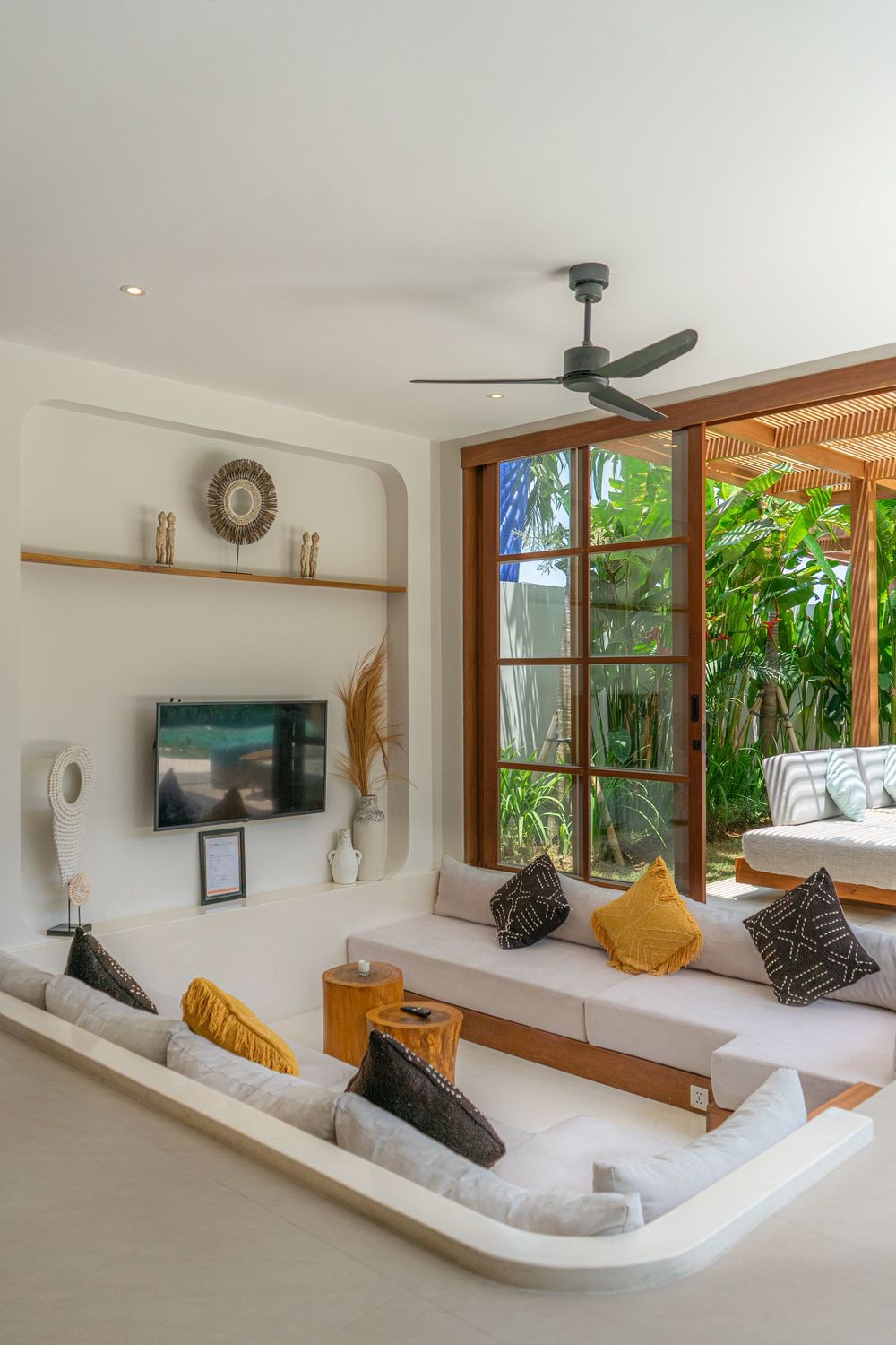 Sunlit villa living room with wooden doors opening to a green garden