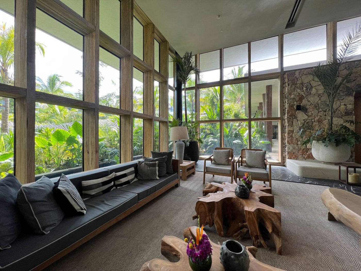 Villa lounge with floor to ceiling wooden framed windows looking onto tropical planting